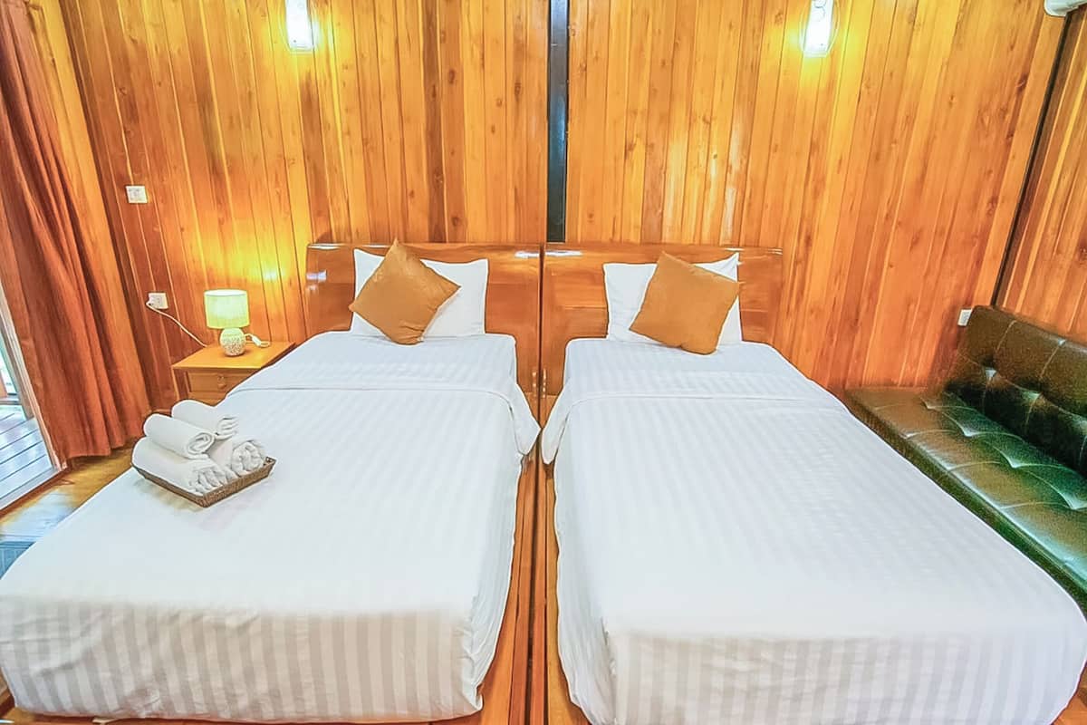 A double room with two beds, wooden paneling, a nightstand with a lamp, and a bench.