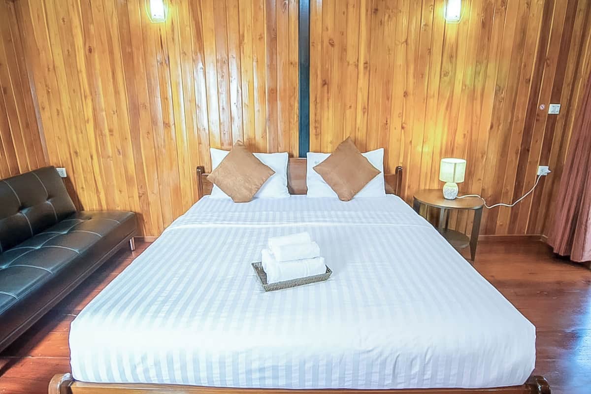 A hotel room with a large bed, two pillows, a bedside table with a lamp, and a wooden wall.