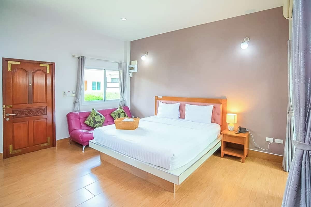 A bedroom with a bed, a nightstand, a wooden door, a window with curtains, and a pink chair.