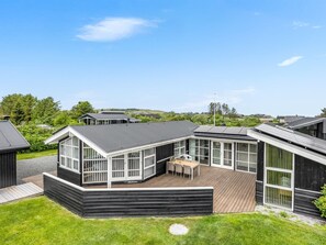 Une maison moderne dotée d’une terrasse, de grandes fenêtres et d’une cour gazonnée.