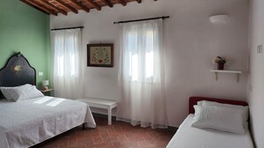 Ein Schlafzimmer mit zwei Betten, einem kleinen Tisch, einem an der Wand befestigten Regal mit Blumen und einem gerahmten Bild.