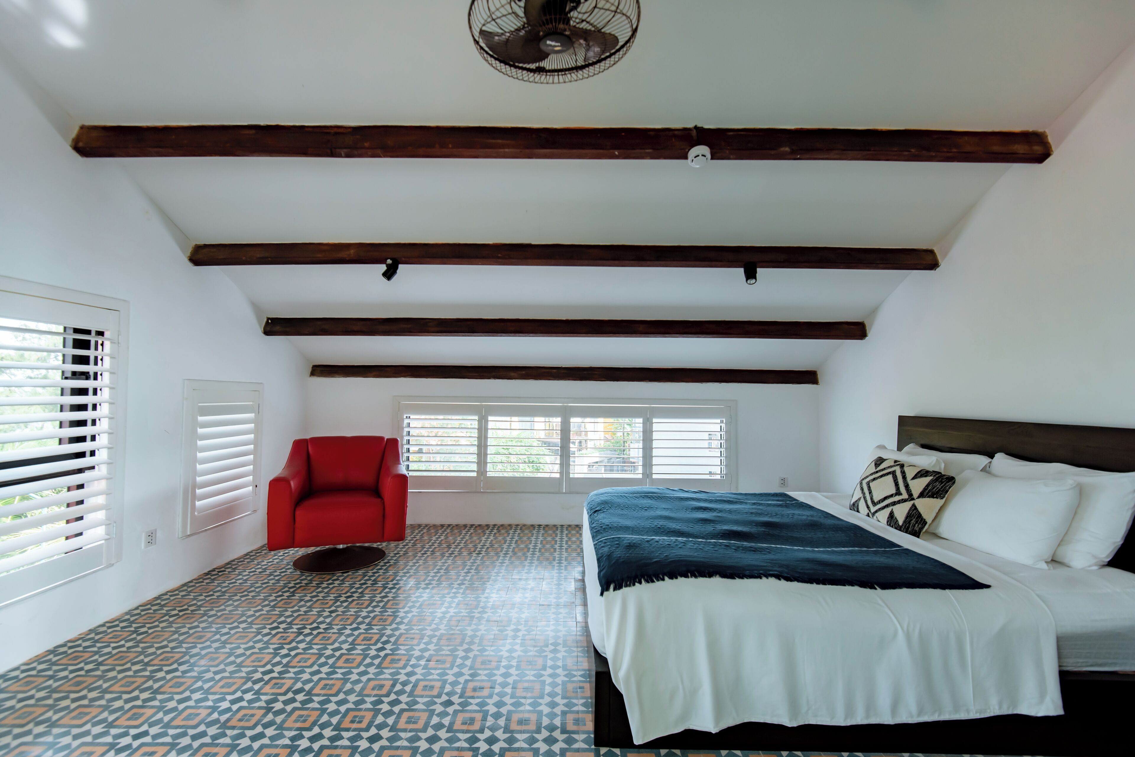 A bedroom with a bed, a red chair, a ceiling fan, and a window with blinds.