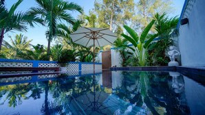 Una piscina cristalina con un muelle de madera, rodeada de exuberante vegetación tropical y una valla de madera.