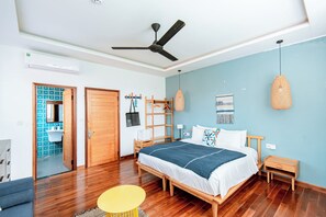 A bedroom with a wooden bed, a ceiling fan, a bedside table, a nightstand, a hanging lamp, and a door leading to a bathroom. - Sea Easter 3BR Seaside An Bang Beach (Da Nang)