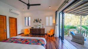 A bedroom with a bed, two chairs, a desk, and a balcony with wicker furniture. - Sea Easter 3BR Seaside An Bang Beach (Da Nang)