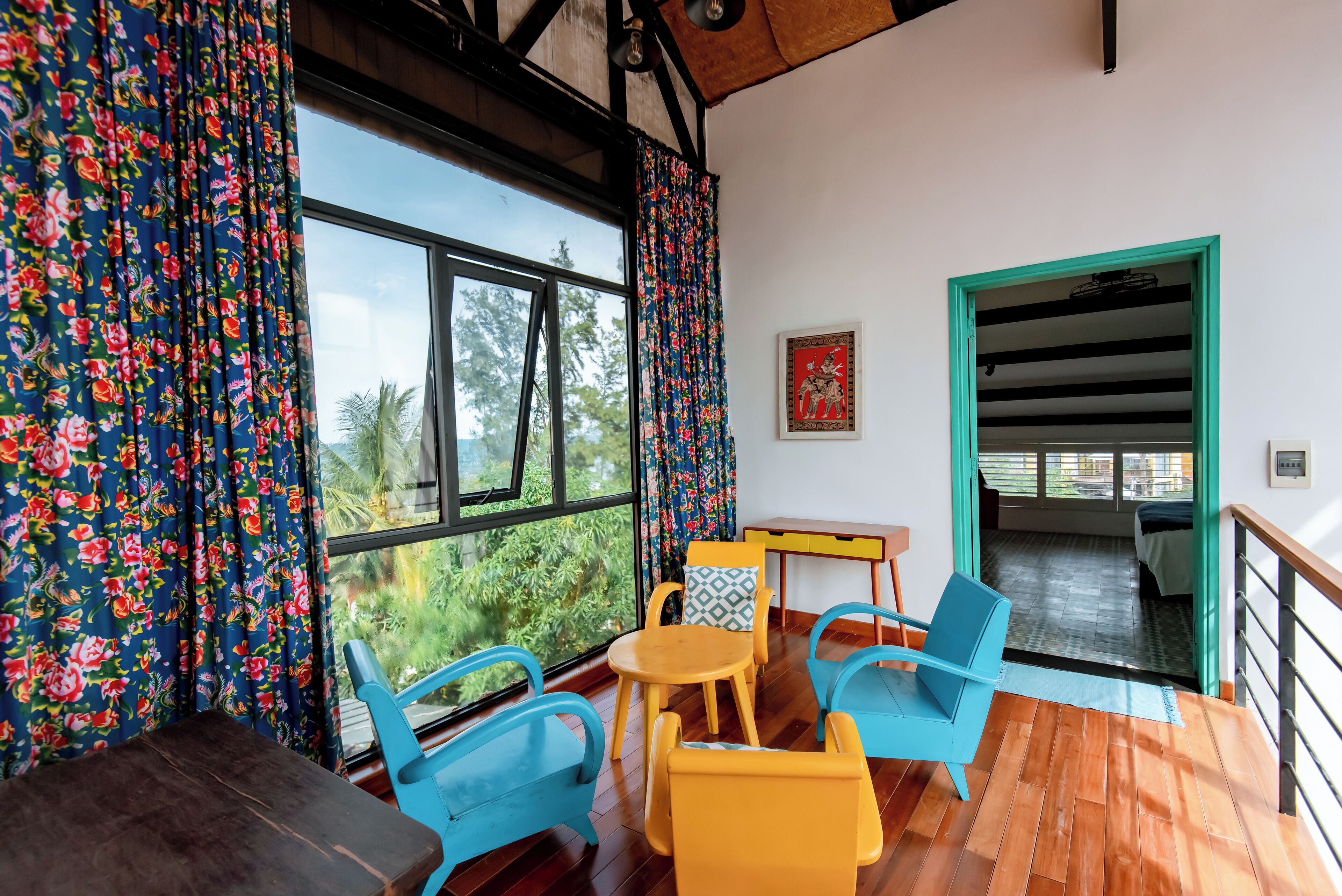 A room with a wooden floor, a table with chairs, and a view of greenery outside.