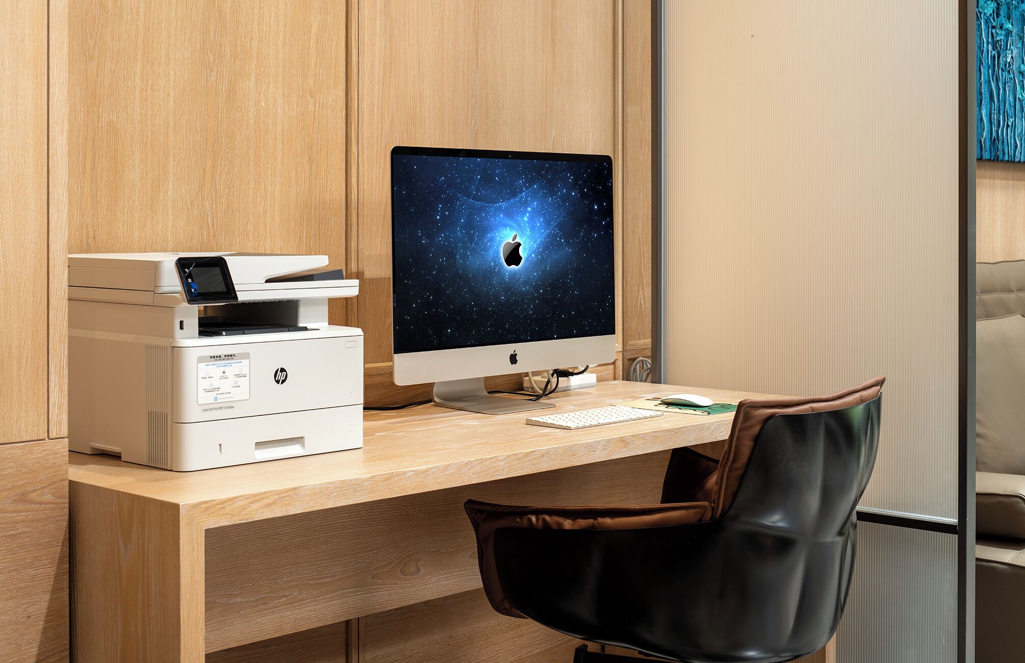 A wooden desk with an HP printer, an Apple iMac, a keyboard, and a leather chair.