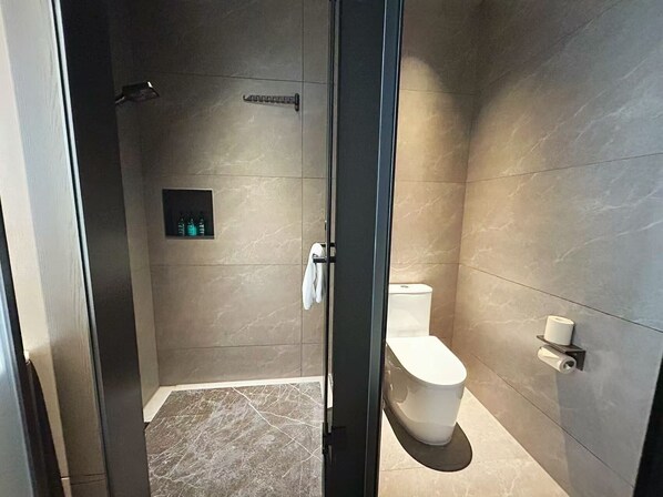 A modern bathroom with a glass shower enclosure, a toilet, and a small shelf with toiletries. - Meihao Lizhi Hotel (Xi'an Lintong Huaqingchi Subway Station Branch) (Xi'an)