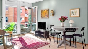 Ein modernes Wohnzimmer mit Essbereich, Fernseher und einem Balkon mit Blick auf Gebäude.