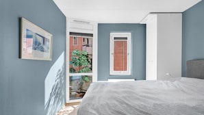 Ein Schlafzimmer mit einem Bett, einer Tür, einem Fenster und einem gerahmten Bild an der Wand.