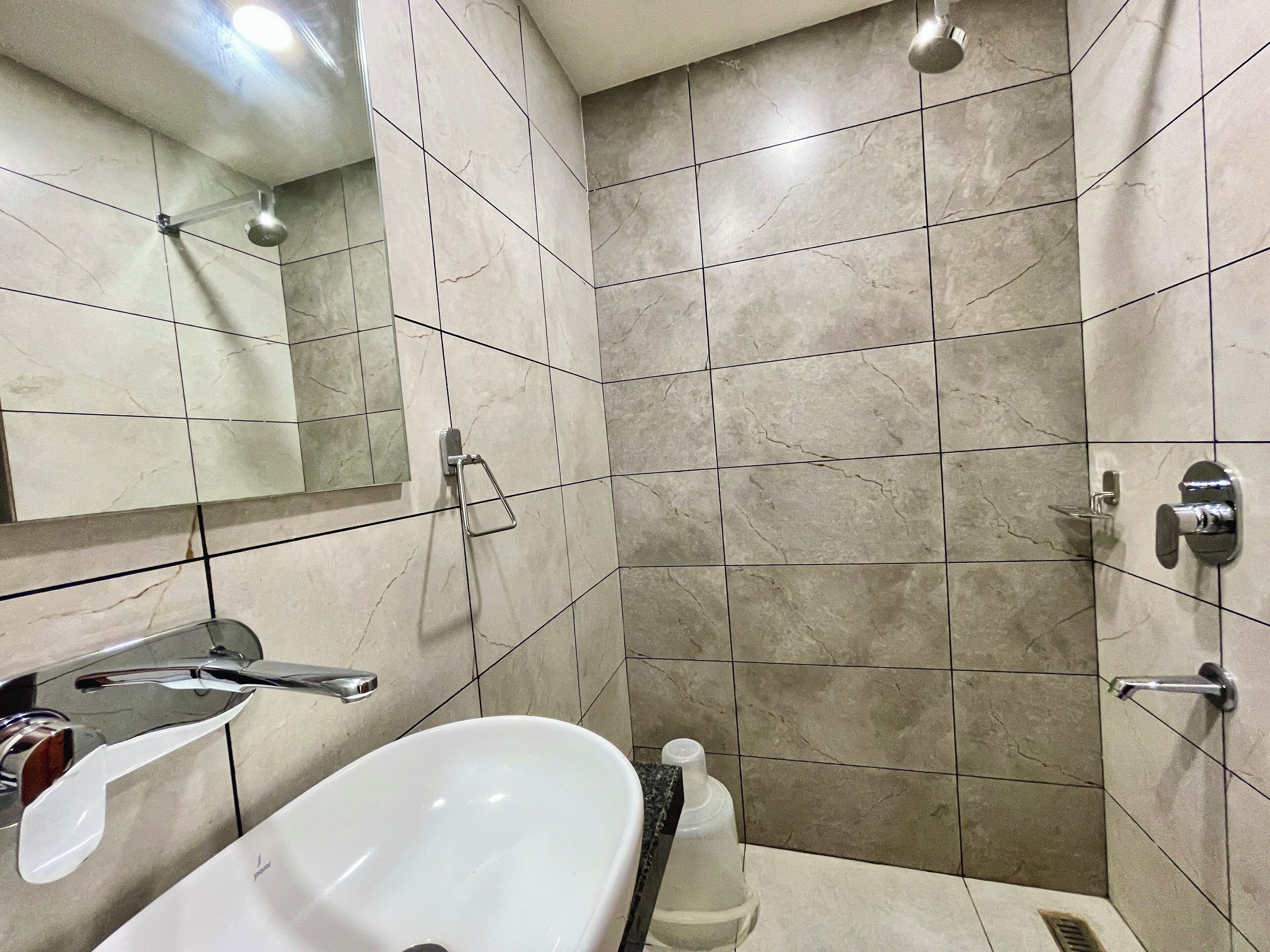 A bathroom with a white sink, a mirror, a shower, and tiled walls.