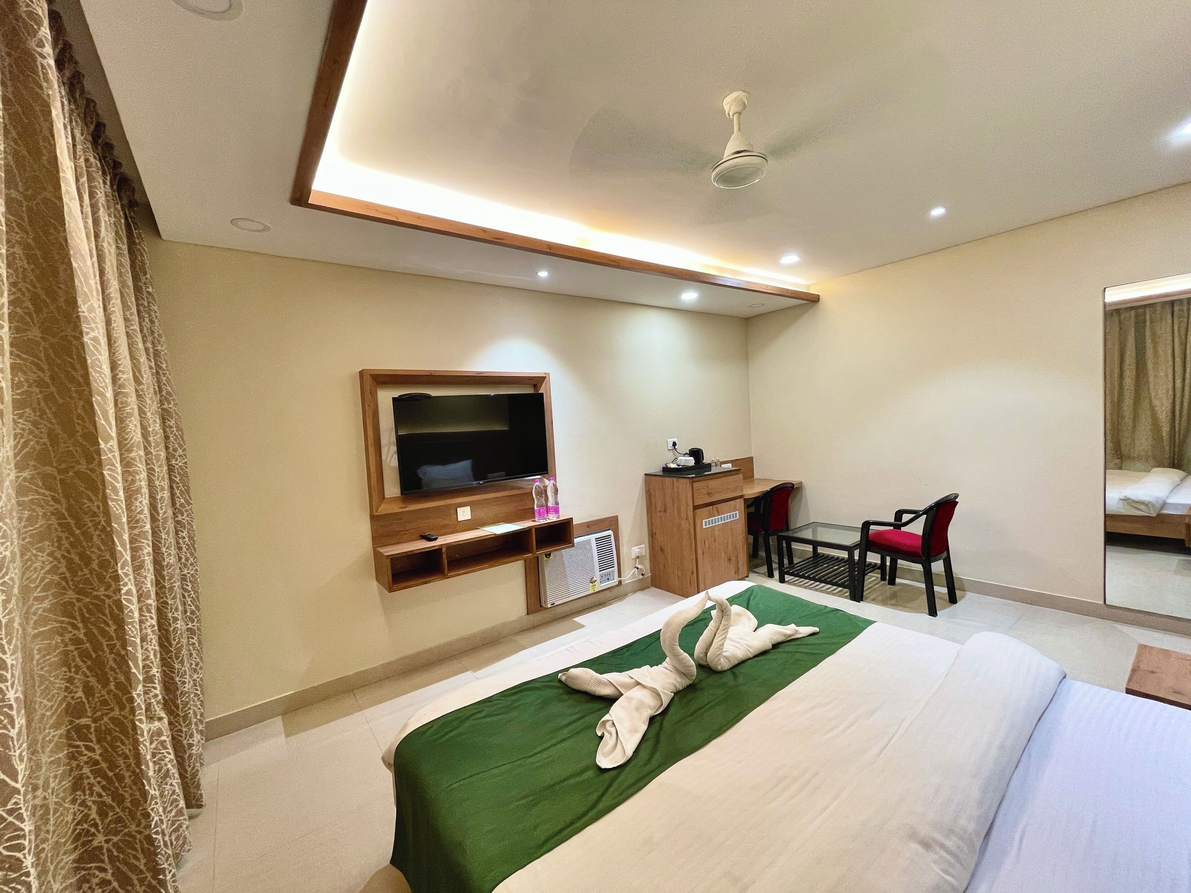 A hotel room with a bed, a desk, a chair, a television, and a ceiling fan.
