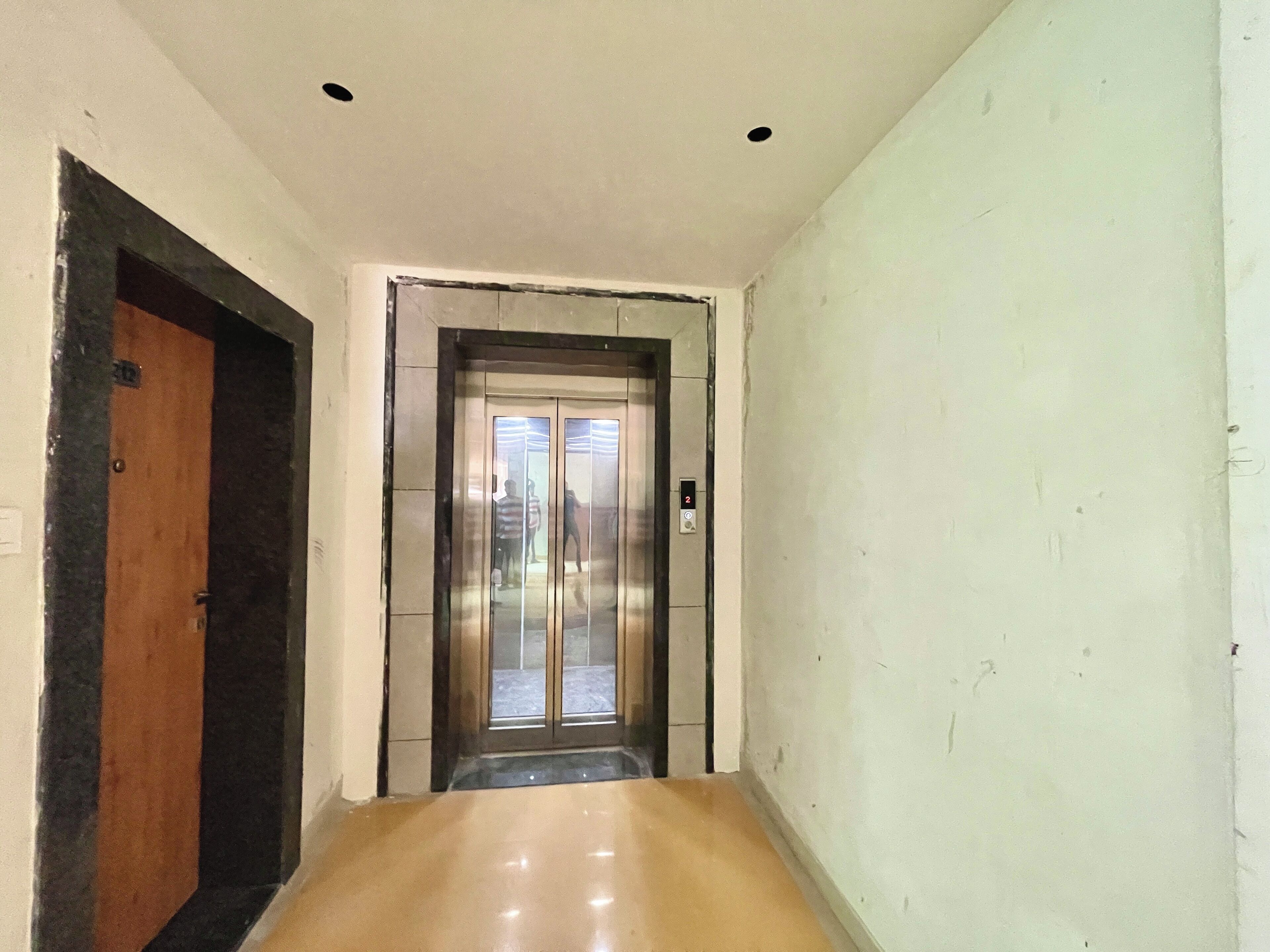 A narrow hallway with a wooden door on the left and an elevator in the center.