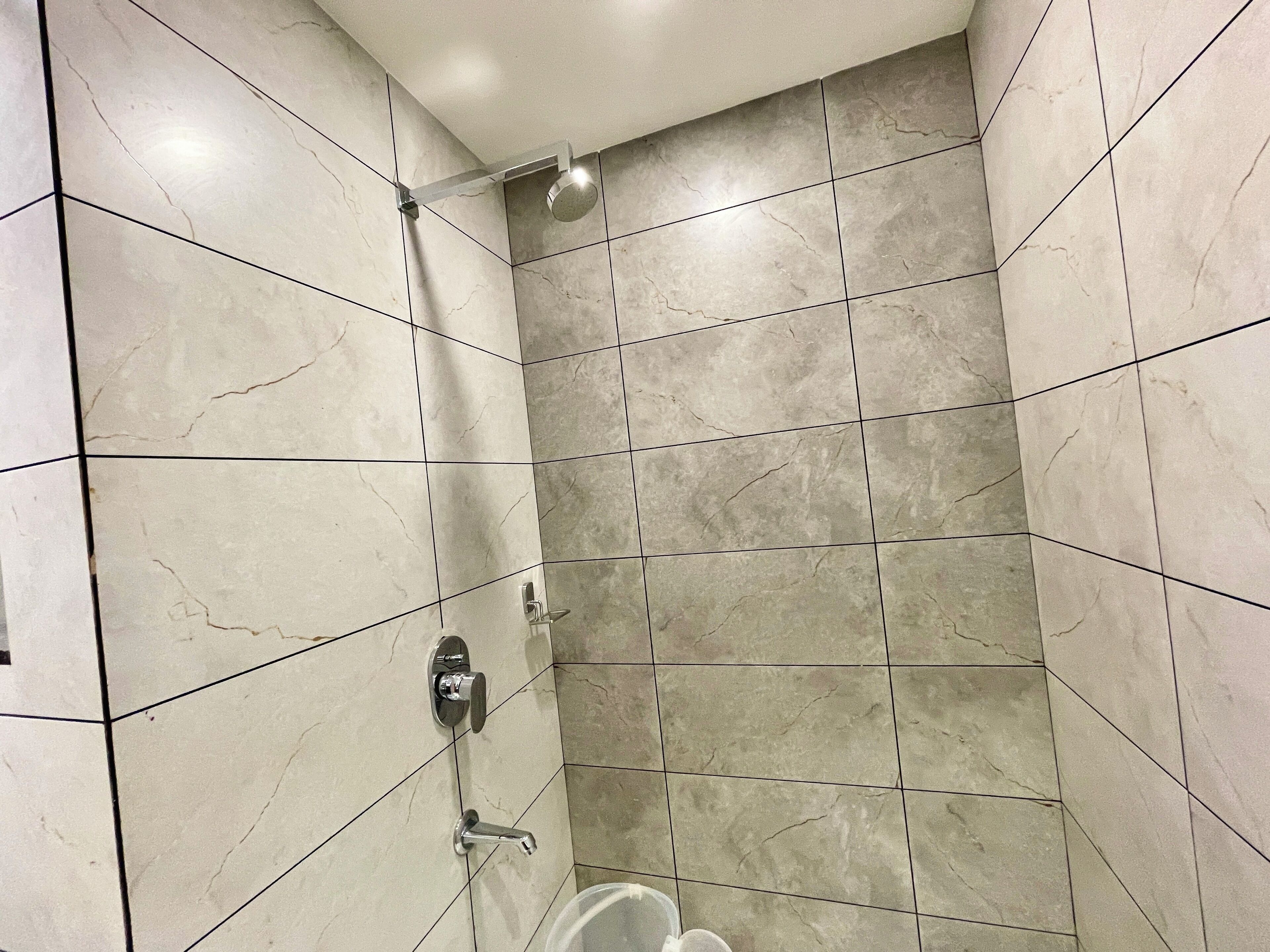 A shower with a handheld showerhead and a wall-mounted faucet in a tiled bathroom.