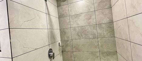 A shower with a handheld showerhead and a wall-mounted faucet in a tiled bathroom.