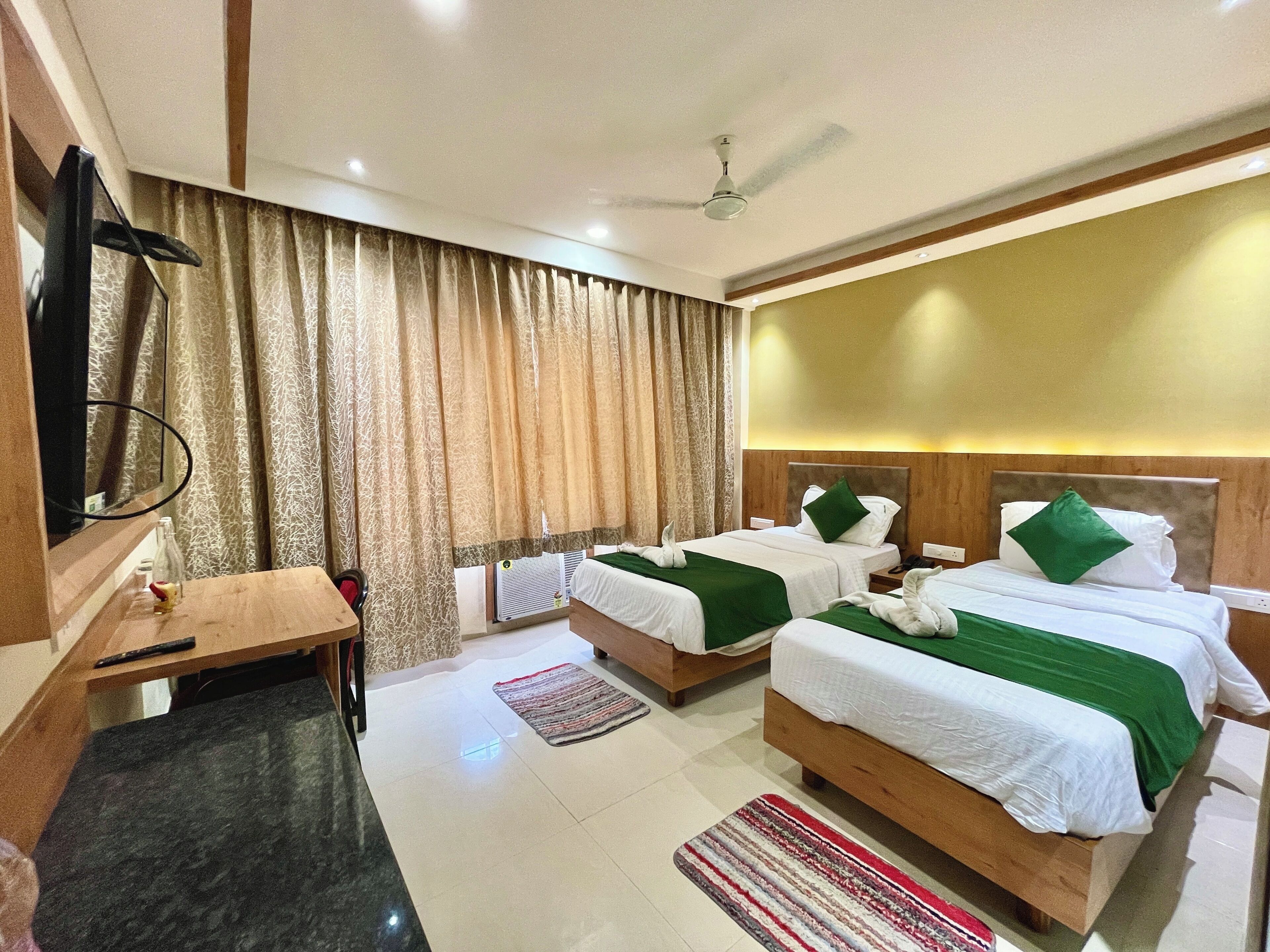 A hotel room with two beds, a desk, a mirror, a ceiling fan, and a large window with curtains.