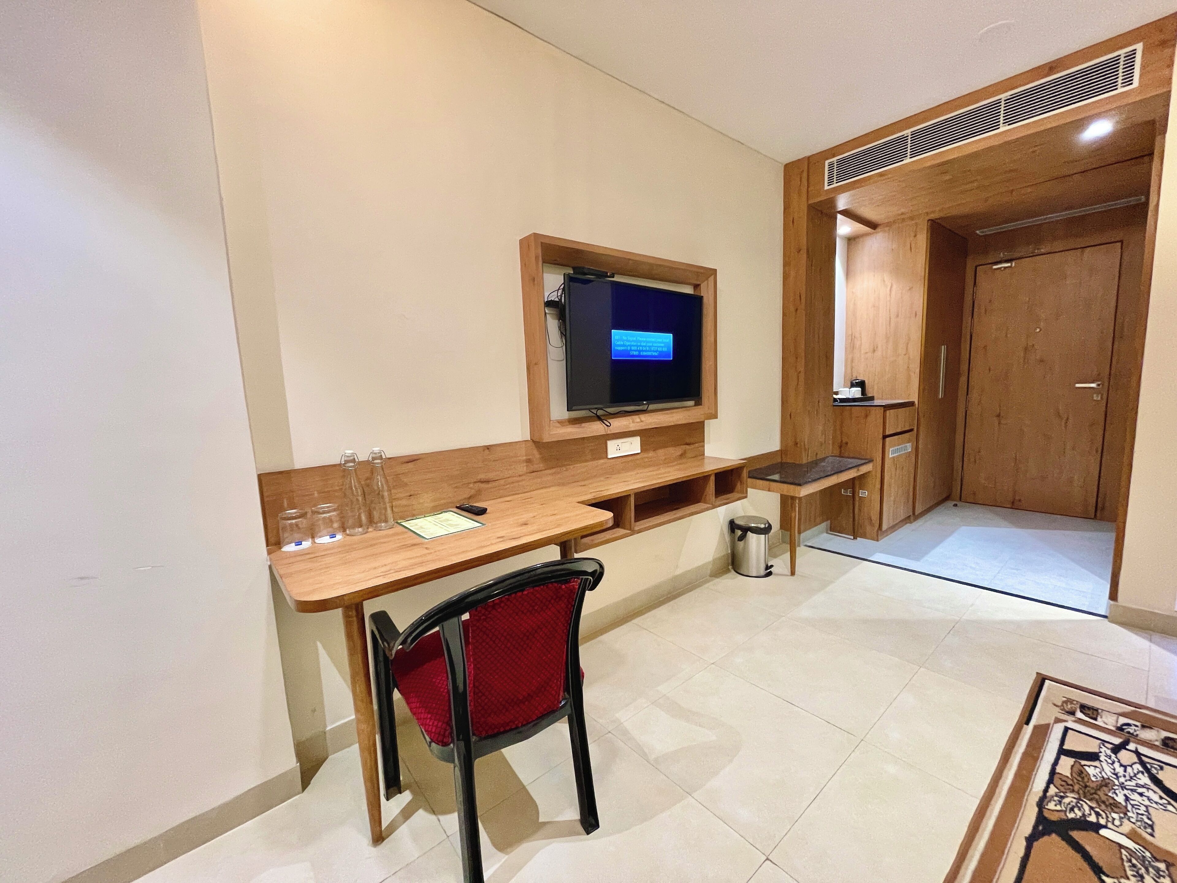Une pièce de taille modeste, avec un bureau en bois, un téléviseur fixé au mur, une chaise rouge et une petite poubelle.