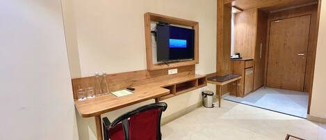 Une pièce de taille modeste, avec un bureau en bois, un téléviseur fixé au mur, une chaise rouge et une petite poubelle.