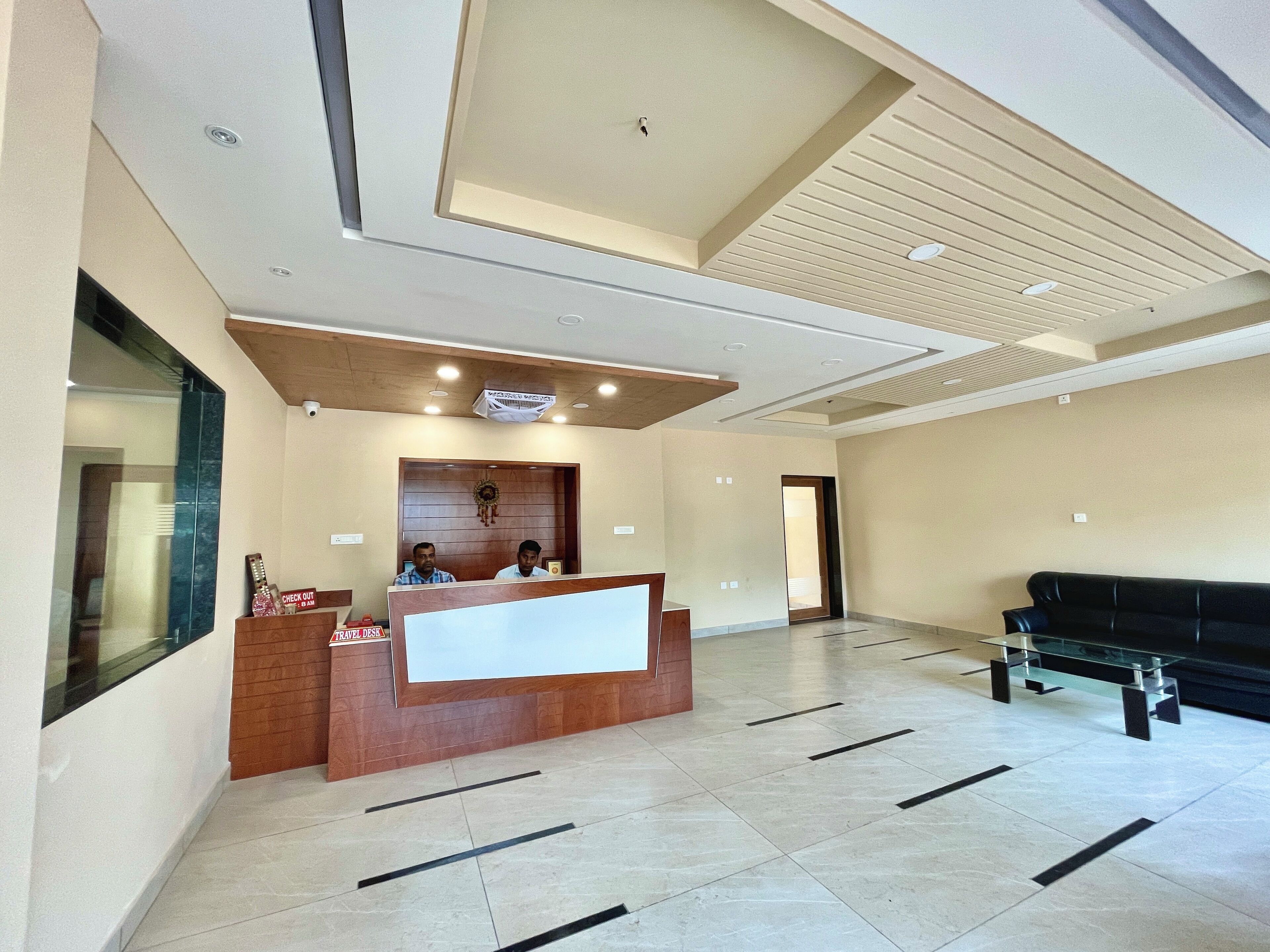 A hotel reception area with a reception desk, a black leather sofa, and a large window.