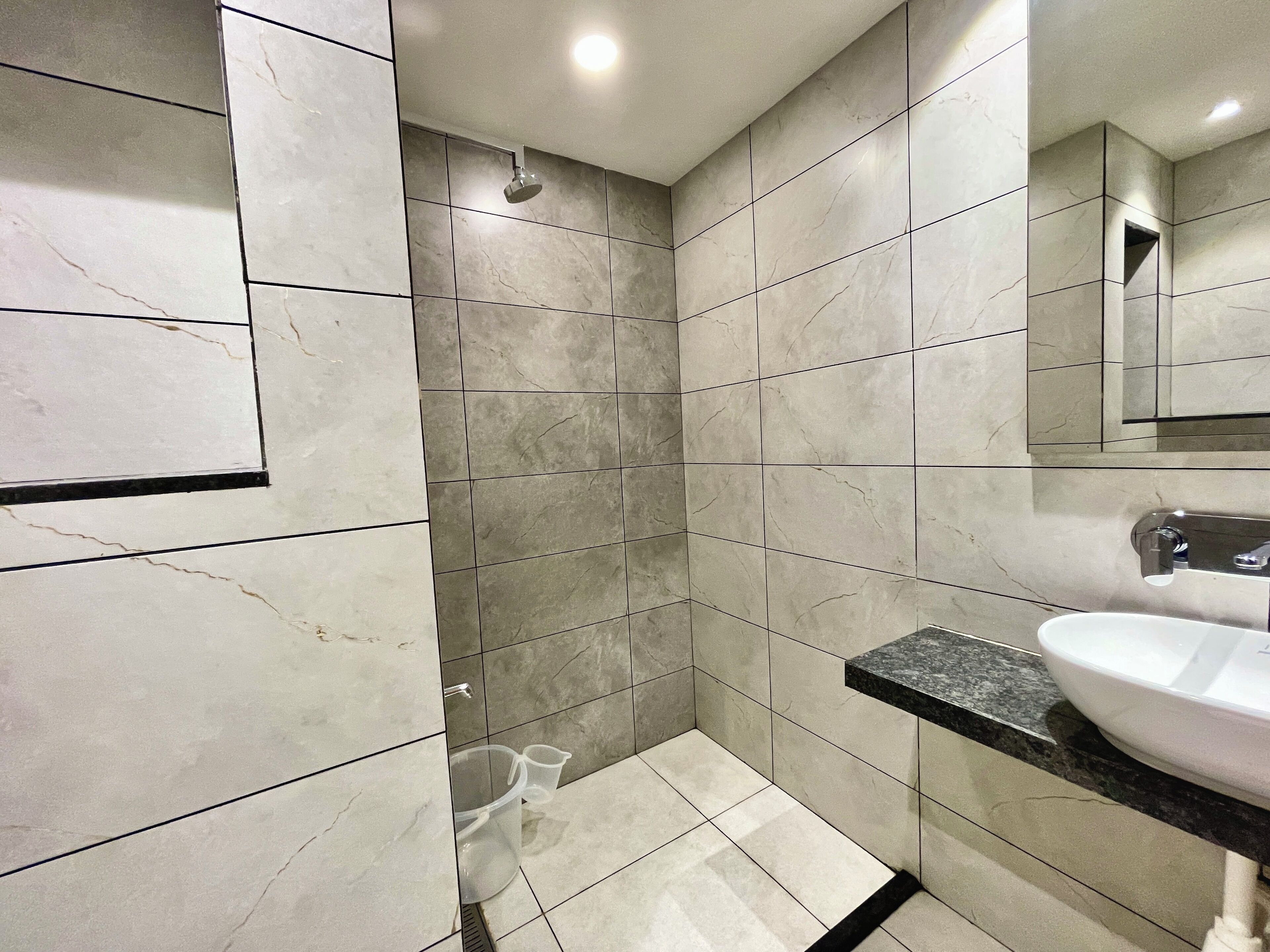 Un baño moderno con baldosas de mármol gris, ducha y lavamanos con encimera negra.