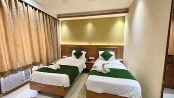 A hotel room with two beds, each with a green bedspread and white linens, a ceiling fan, and a large window with curtains.