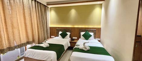 A hotel room with two beds, each with a green bedspread and white linens, a ceiling fan, and a large window with curtains.