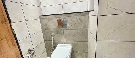 A small, tiled bathroom with a toilet, a shower, and a hand dryer.