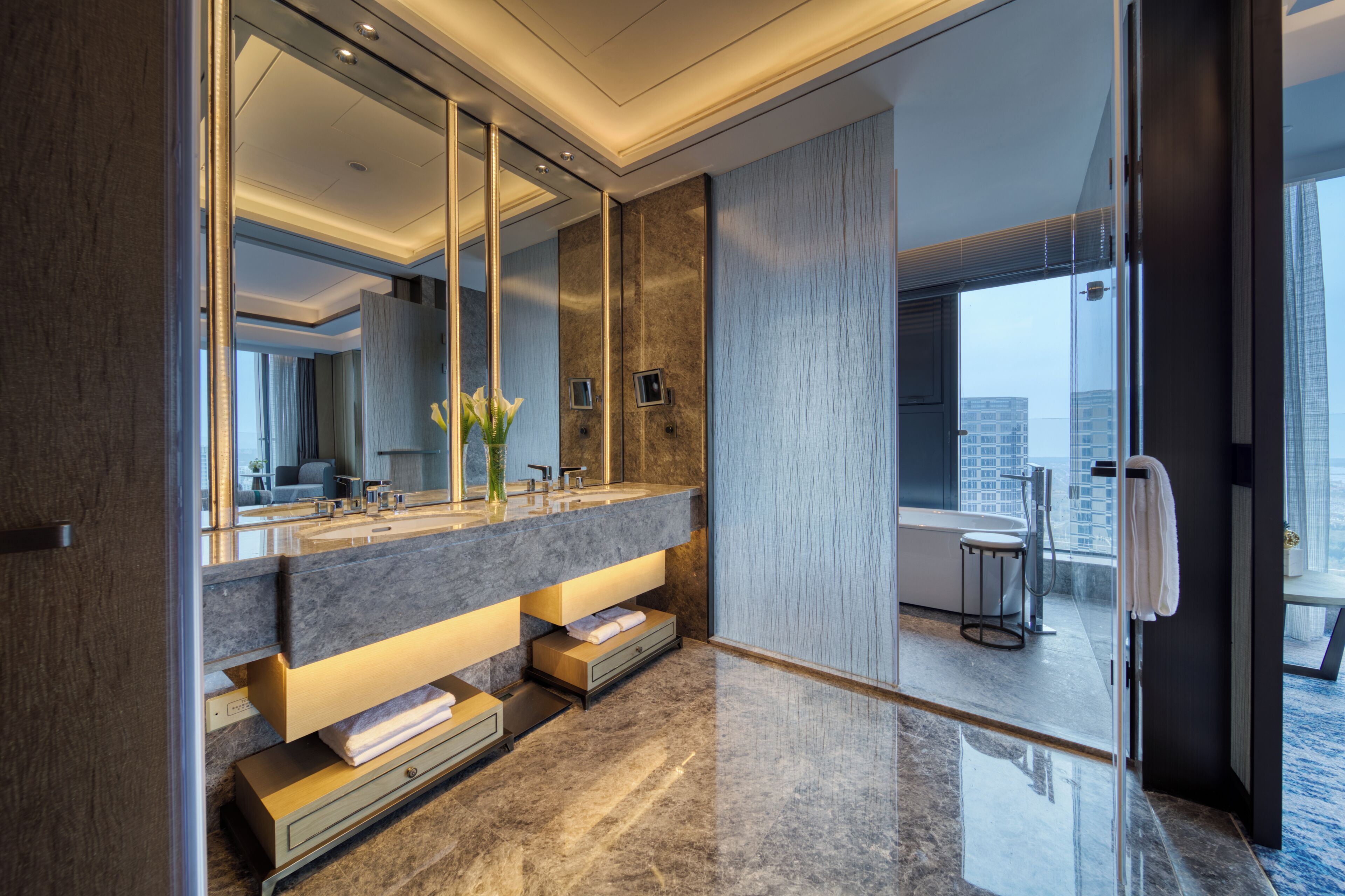 Un bagno moderno con uno specchio grande, un mobile lavabo con piano in marmo e vista sulla città.