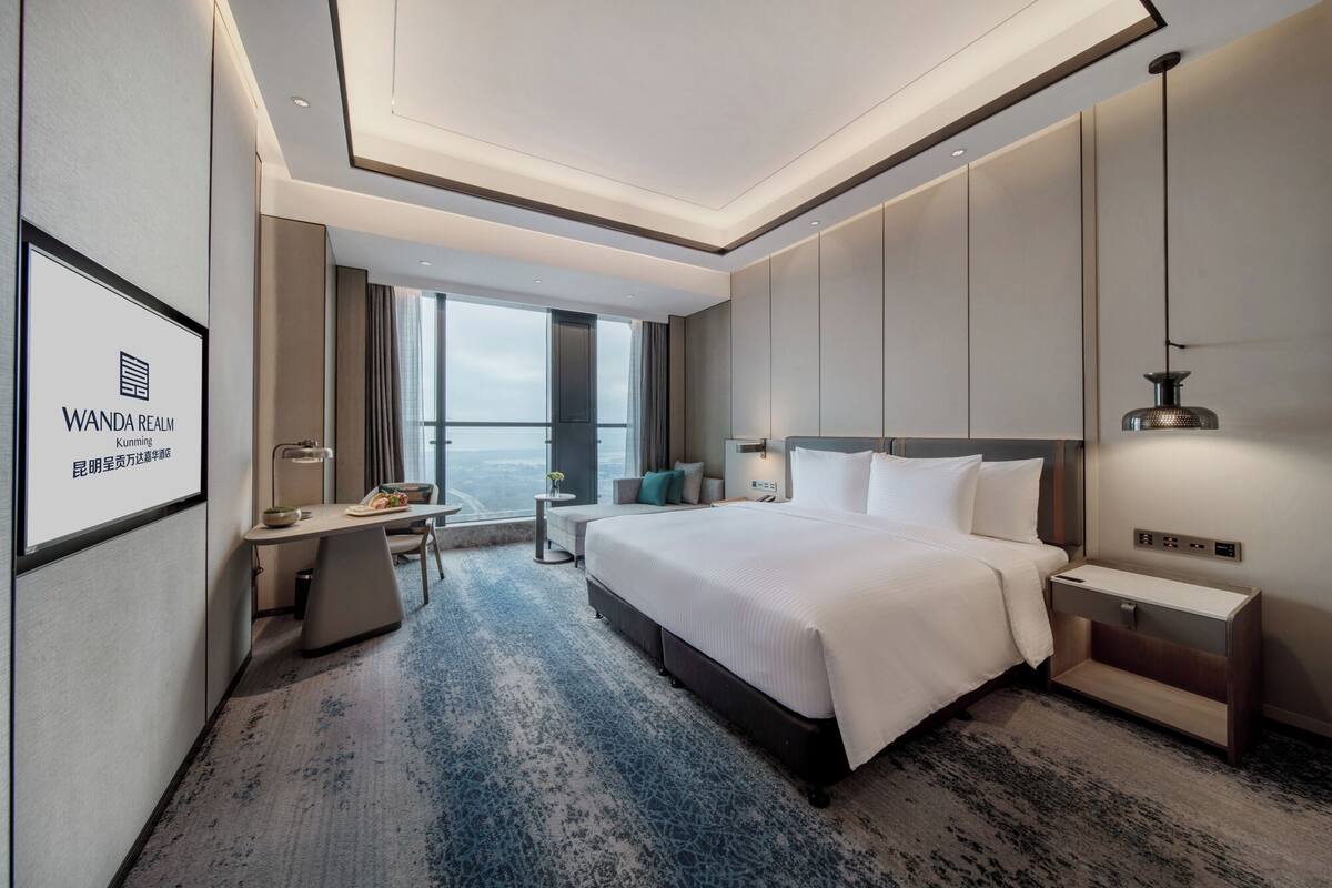 A modern hotel room with a large bed, a desk, and a view of the city.