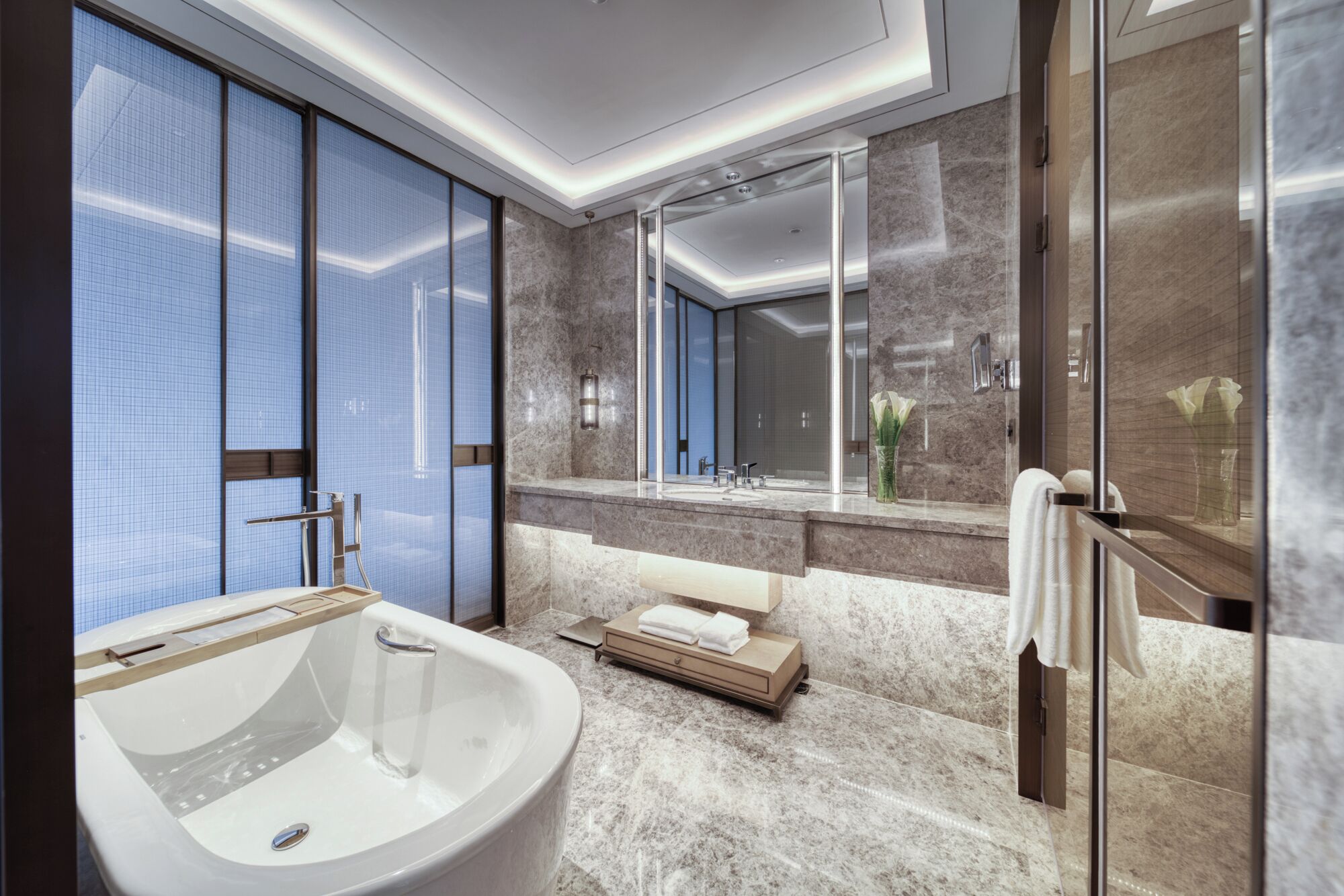 A modern bathroom with a large bathtub, a glass shower enclosure, and a marble-tiled floor.