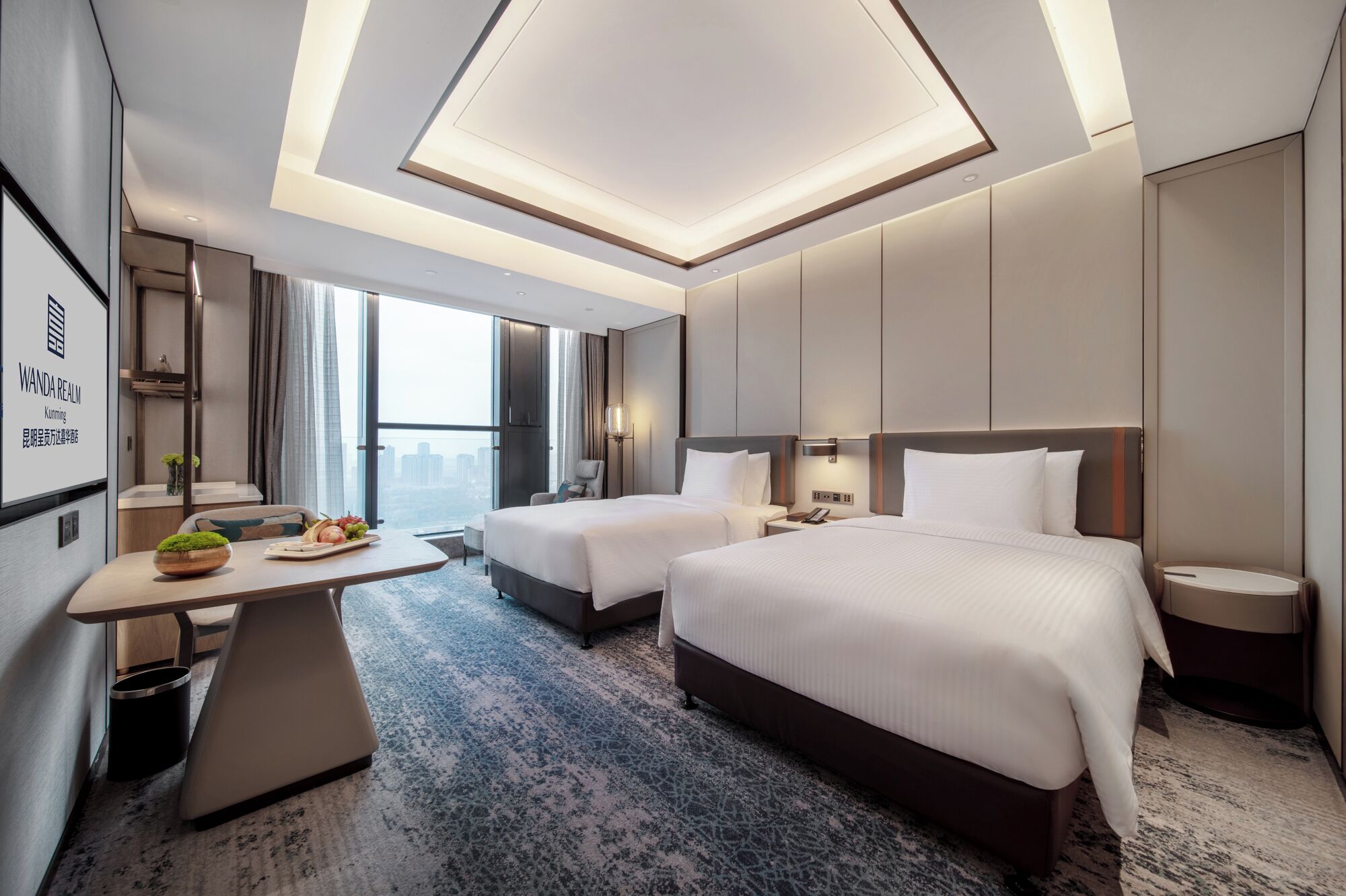 A modern hotel room with two beds, a desk, and a large window offering a city view.