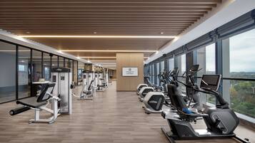 Une salle de sport moderne équipée de divers appareils d’exercice, de grandes fenêtres offrant une vue dégagée et d’un plafond en bois.
