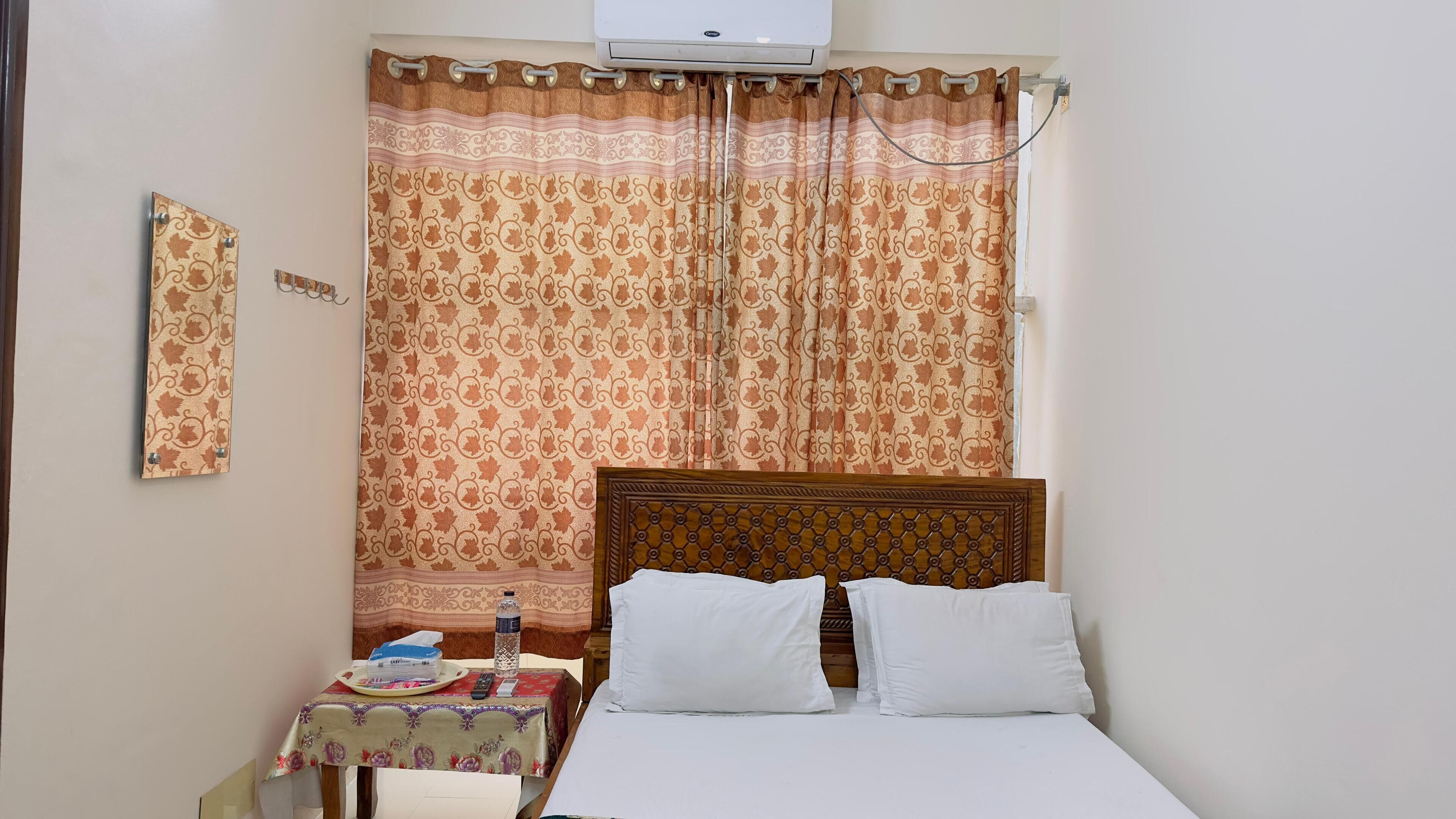 A bedroom with a wooden headboard, a bed with white linens, a small table with a tray and items, and a patterned curtain.