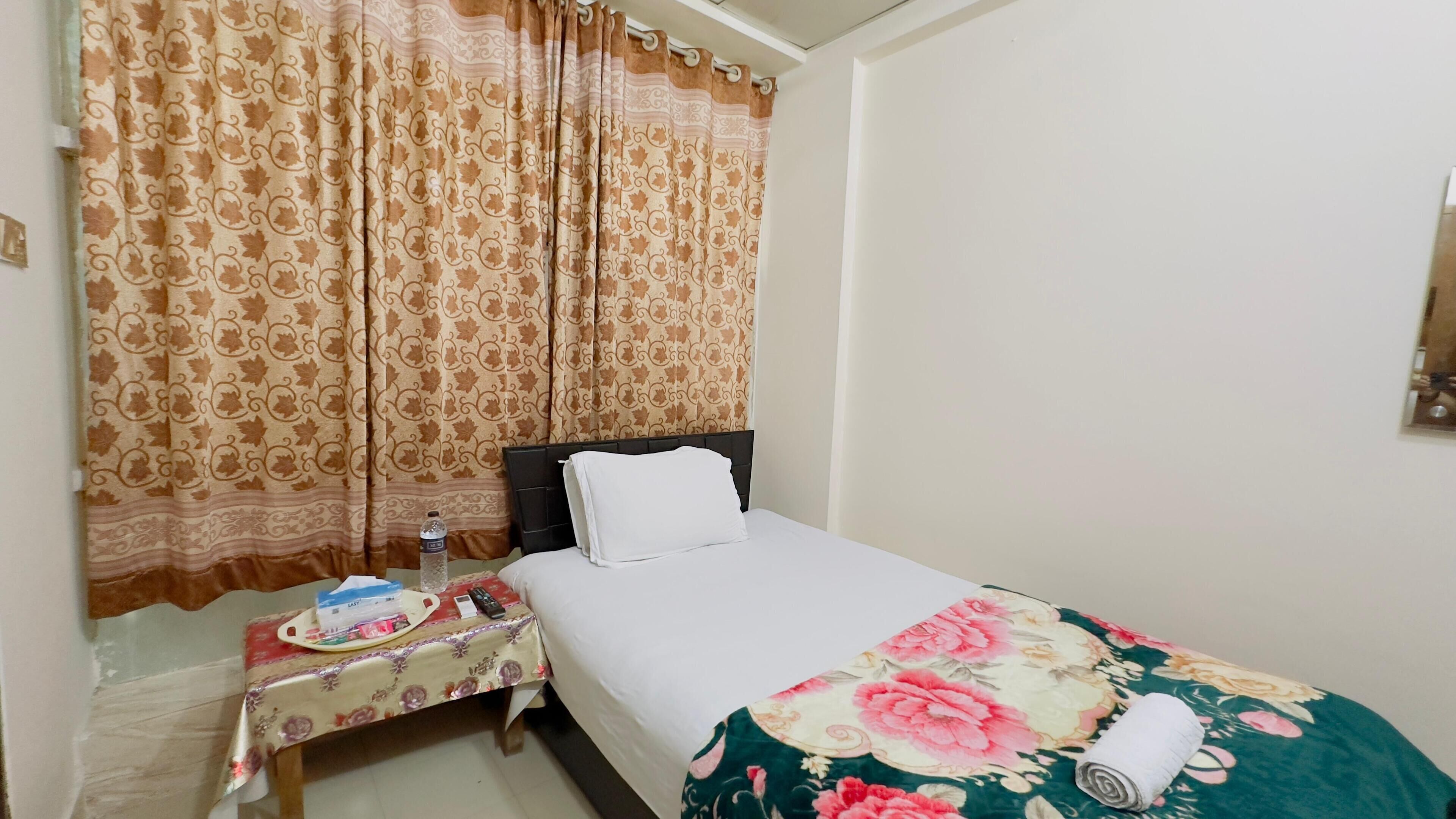 A hotel room with a bed, a nightstand, a water bottle, a remote control, and a floral bedspread.