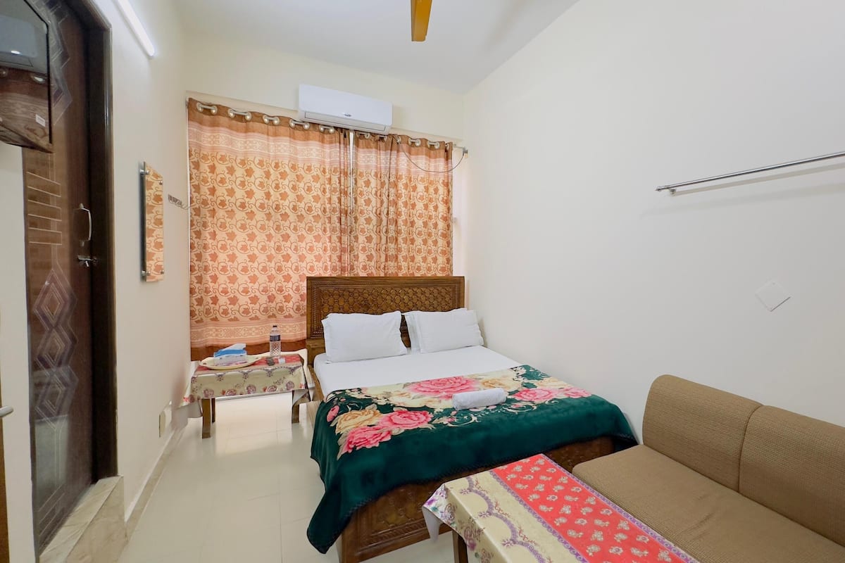 Un dormitorio con cama, mesita de noche, sofá, ventana con cortinas y un equipo de aire acondicionado.