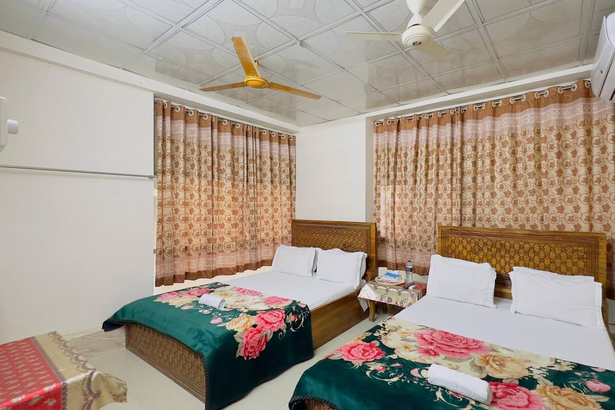 Habitación de hotel con dos camas, cubrecamas estampados con motivos florales, ventilador de techo y cortinas con diseño.