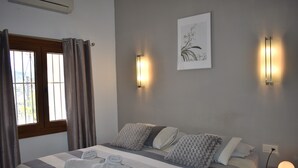 Een slaapkamer met een bed, kussens, een nachtkastje met een lamp en een raam met gordijnen.