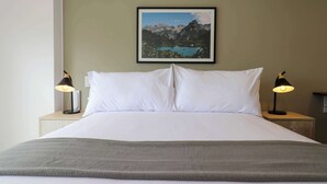 A neatly made bed with white linens and a gray throw blanket, two bedside lamps, and a framed picture of a mountain landscape on the wall. - w* | Fabulous 2BR w/ Balcony in Miraflores (Miraflores)