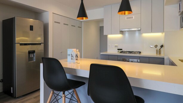 A modern kitchen with a stainless steel refrigerator, two black chairs, and pendant lighting. - w* | Fabulous 2BR w/ Balcony in Miraflores (Miraflores)