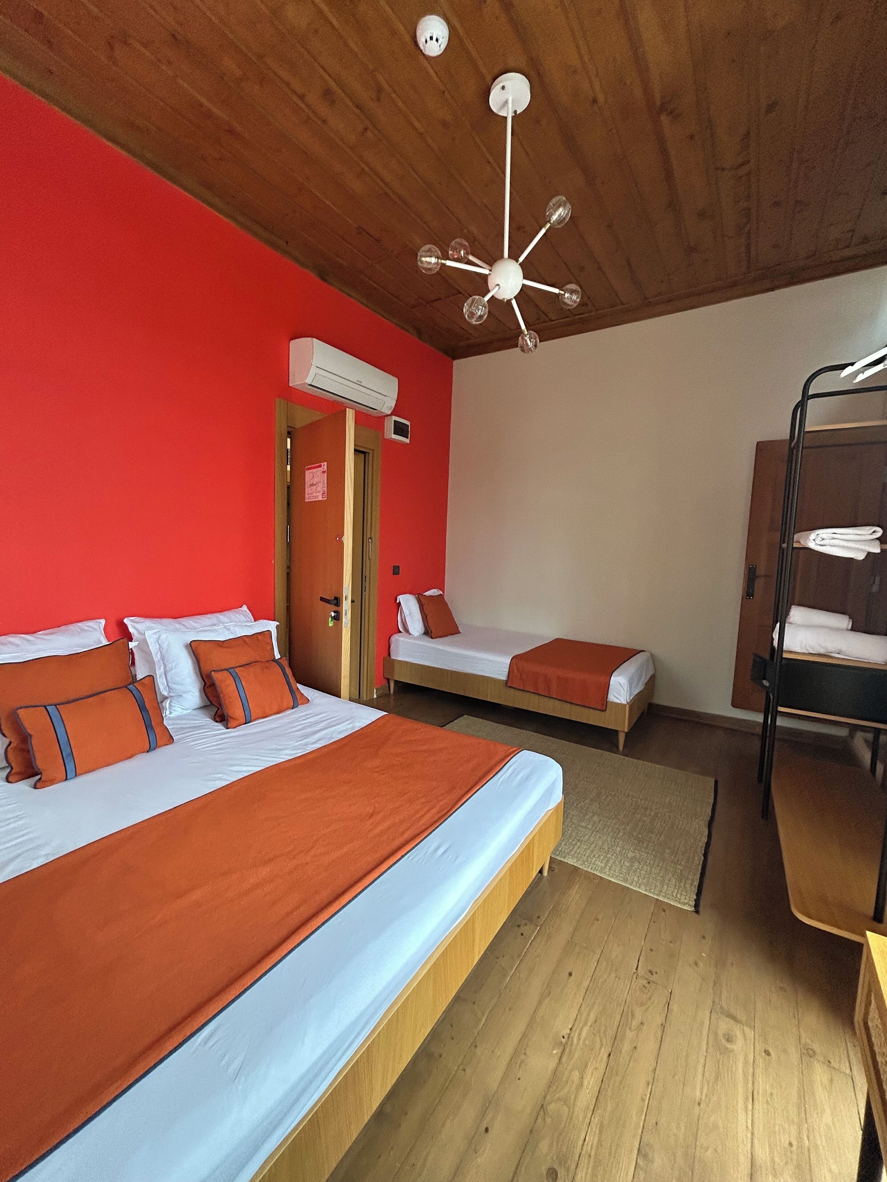 A room with two beds, a bunk bed, a wooden ceiling, and a ceiling fan.