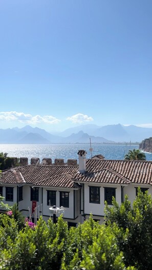 A coastal view with terracotta-tiled buildings, a clear sky, and distant mountains. - Oldies Hotel Bistro Restaurant (Antalya)