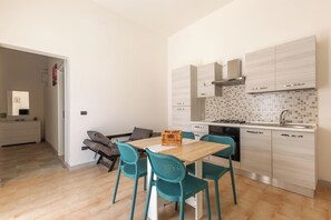 A modern kitchen with light wood cabinets, a tiled backsplash, and a dining area with a wooden table and teal chairs. - 4137 Villetta del Chidro by Barbarhouse (Manduria)