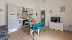 Une cuisine compacte dotée d’appareils électroménagers modernes, un coin repas avec des chaises de couleur turquoise et un téléviseur posé sur un meuble blanc.