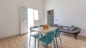 Une pièce comprenant une table en bois, quatre chaises de couleur turquoise, un canapé avec des coussins et une porte donnant sur une autre pièce.