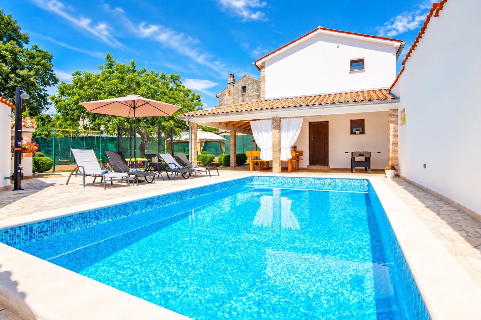 Une piscine avec des chaises longues et des parasols, un espace de repos couvert et un bâtiment doté d’un toit en tuiles.