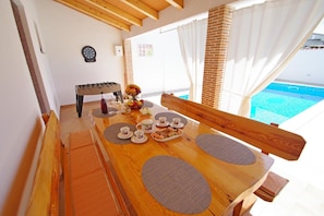 A dining area with a wooden table set for breakfast, including plates, cups, and a fruit bowl. - Charming 3-bedroom house with private pool and beautiful garden (Šajini)