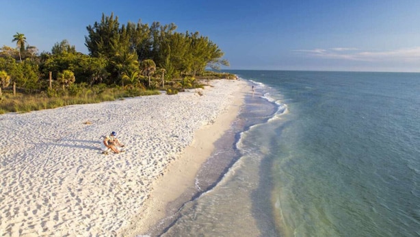 Ein Sandstrand mit klarem türkisblauem Wasser, wenigen Personen und dichter Vegetation entlang der Küste.