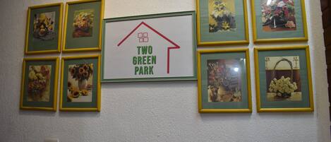 Un mur orné de photographies de fleurs encadrées et sur lequel est apposée une enseigne centrale indiquant « TWO GREEN PARK ».