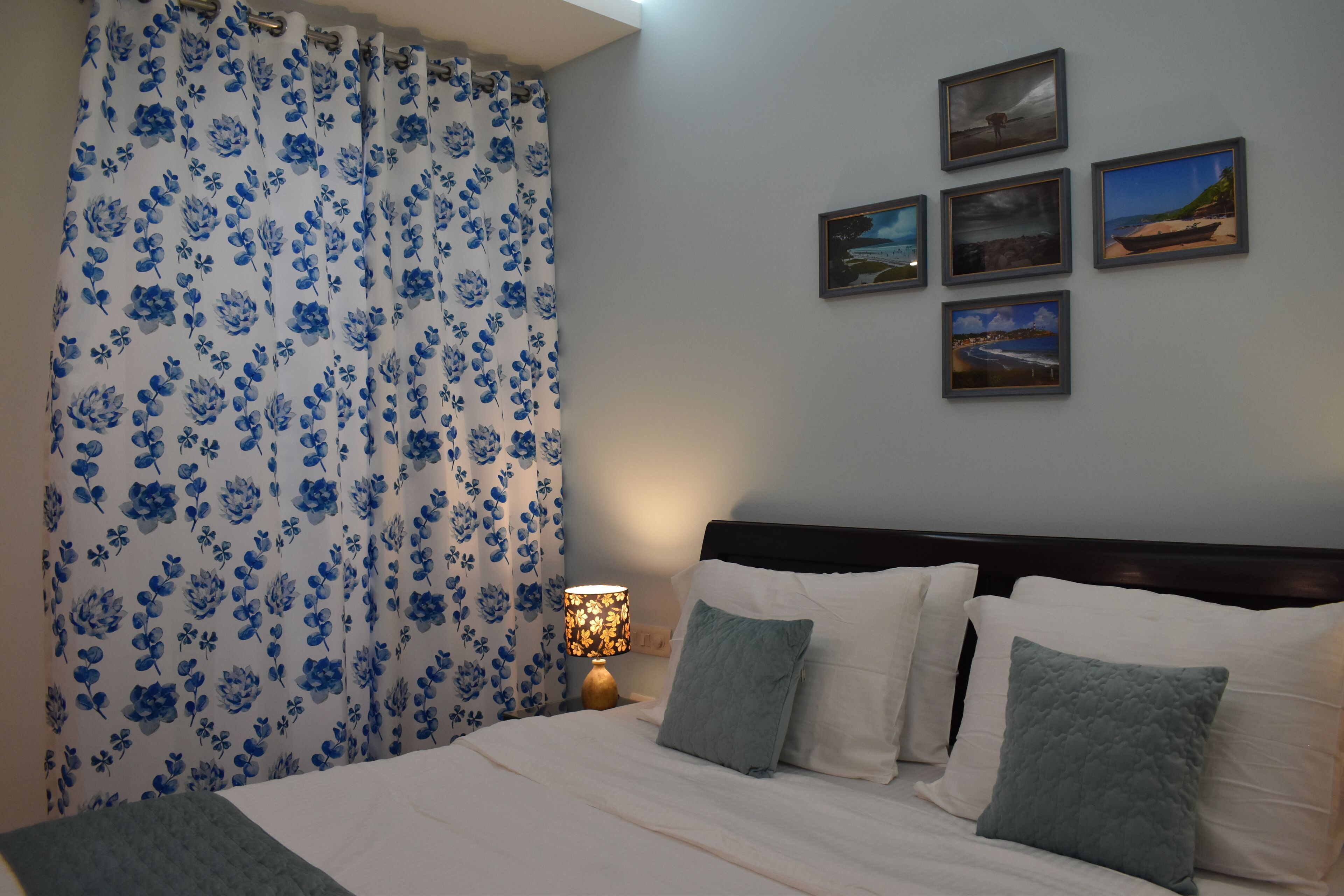 A neatly made bed with white linens and two pillows, a nightstand with a lamp, and a wall with five framed pictures.