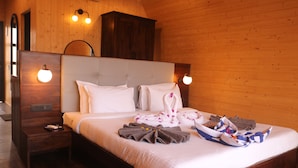Habitación de hotel con interior de madera, una cama grande con ropa blanca, una mesita de noche con lámpara y un armario de madera.